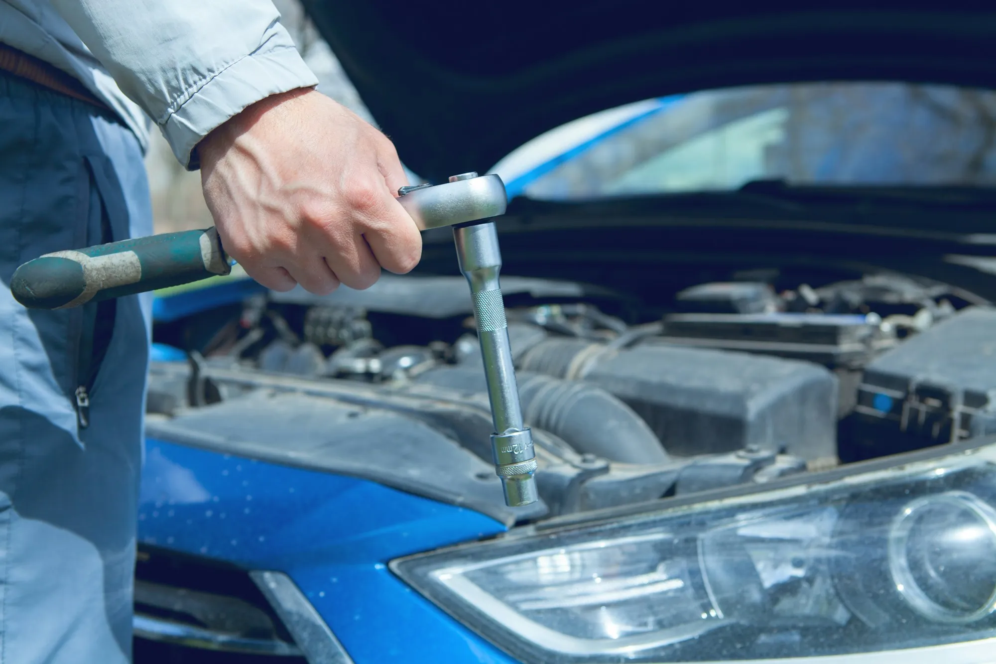 Technician leaning over the engine bay of a blue car with a ratchet